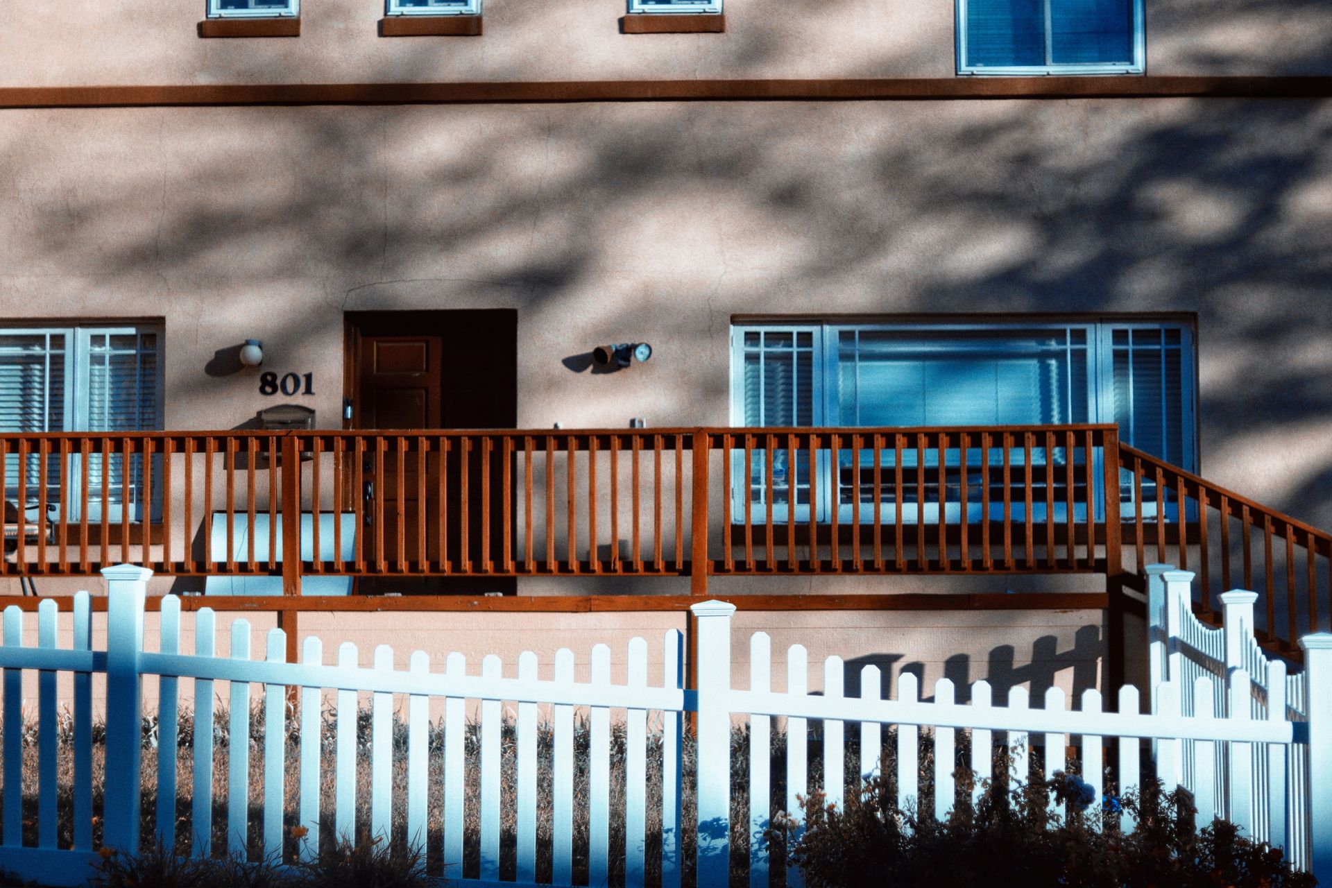 Modern house facade with a wood balcony and white picket fence in daylight.