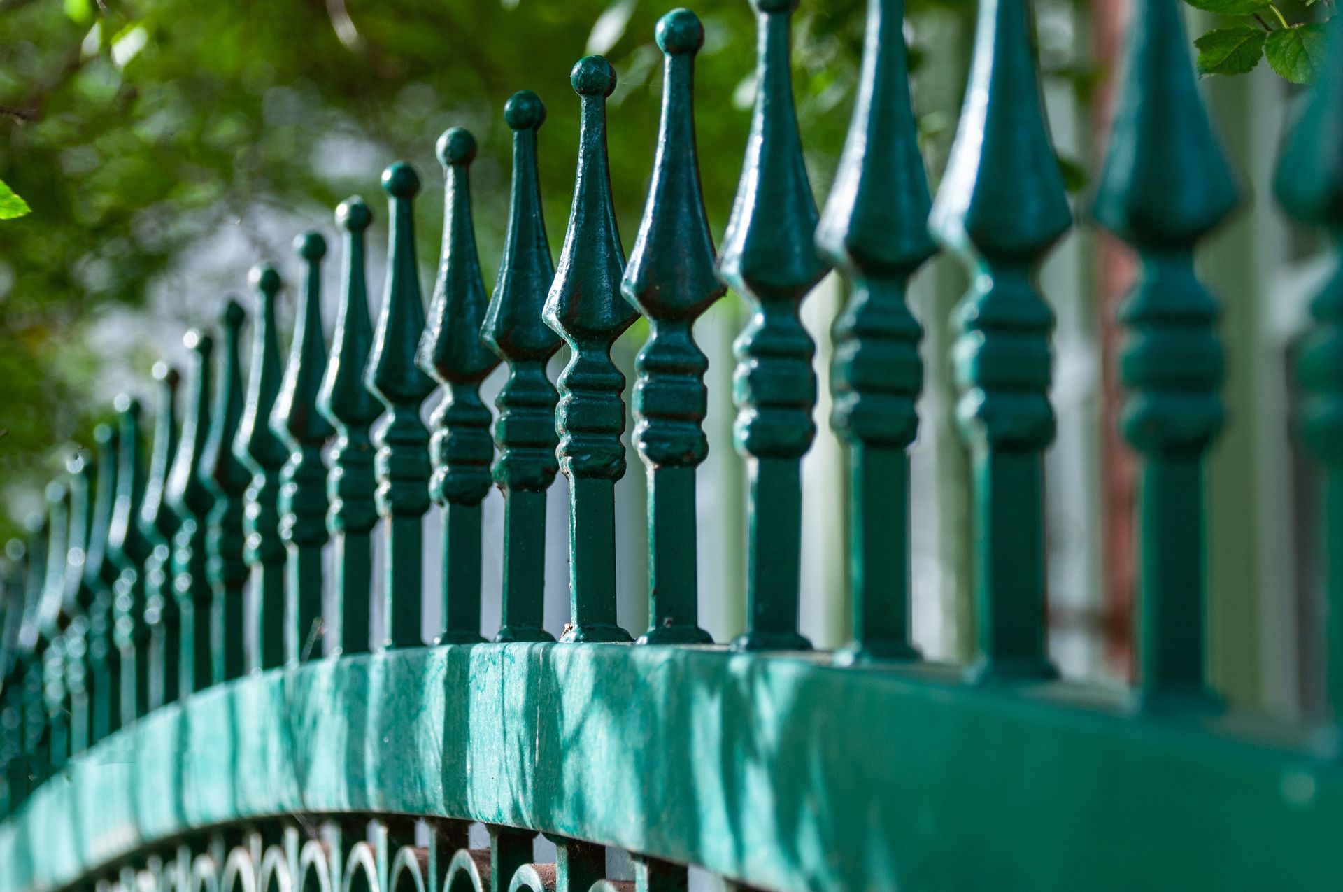Detailed view of a decorative green iron fence with focus on intricate design elements.