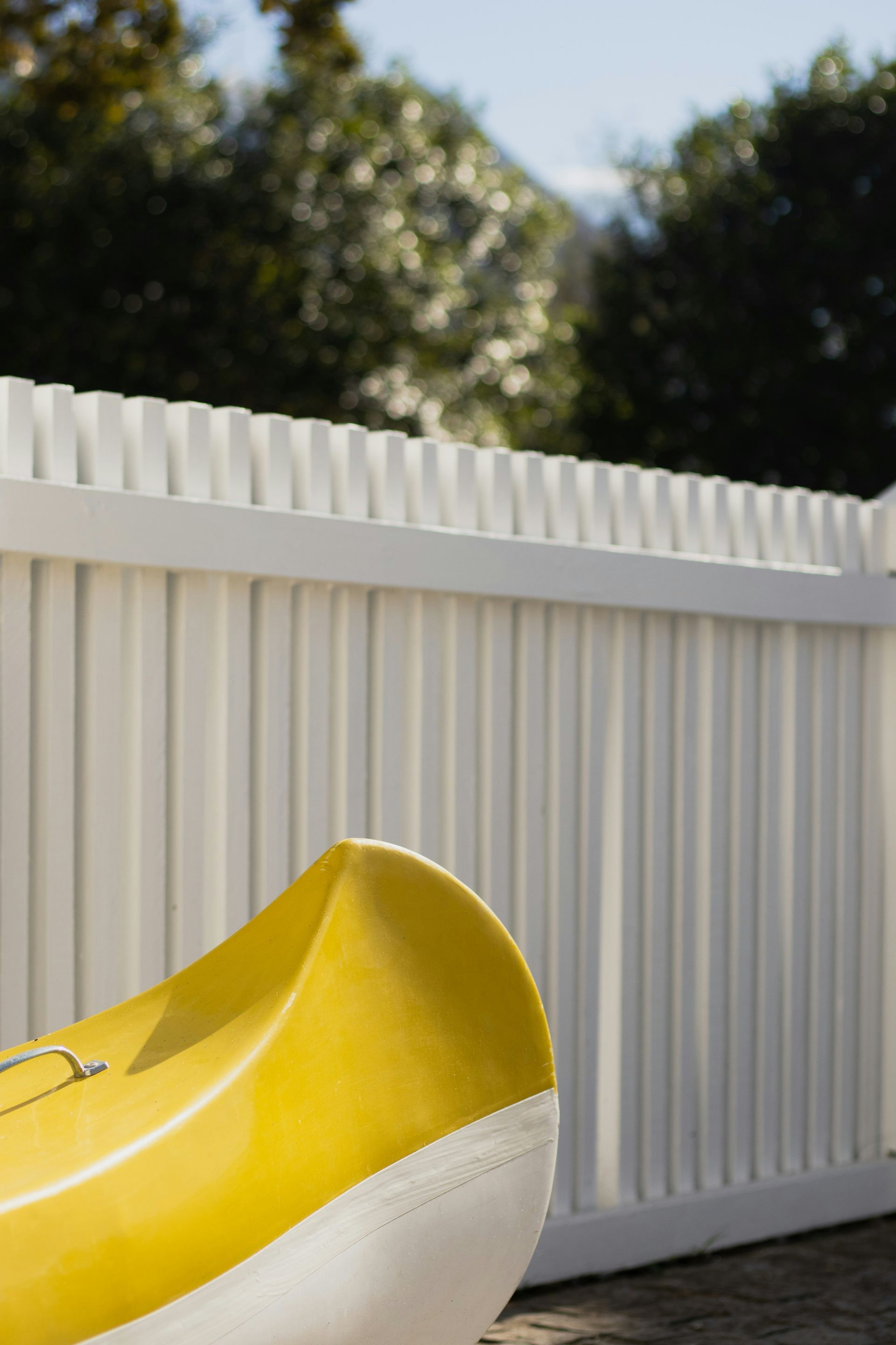 A yellow and white boat sitting next to a white fence